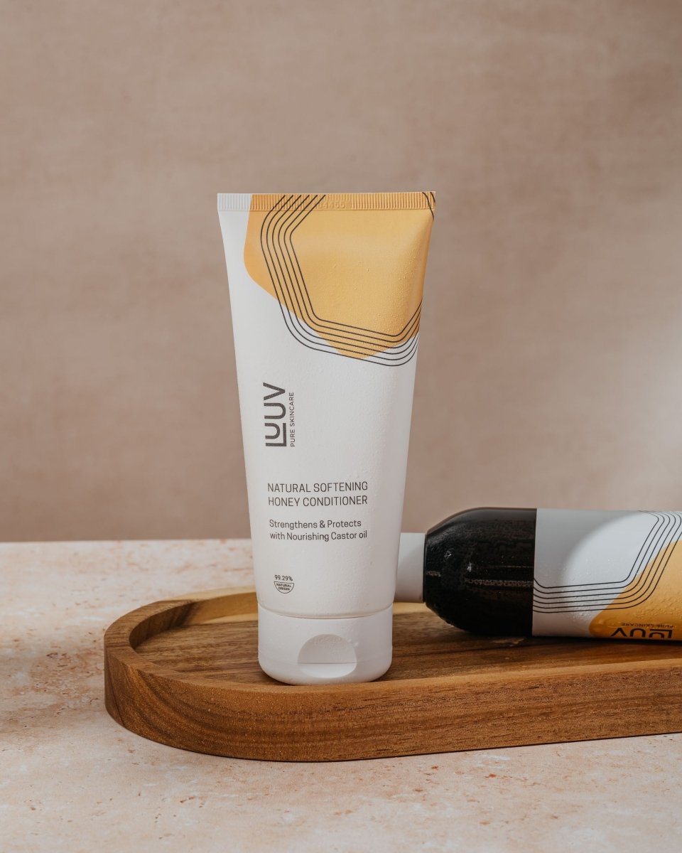 LUUV Natural Softening Honey Conditioner i vit tub med guldorange design, står på träbricka bredvid svart sten