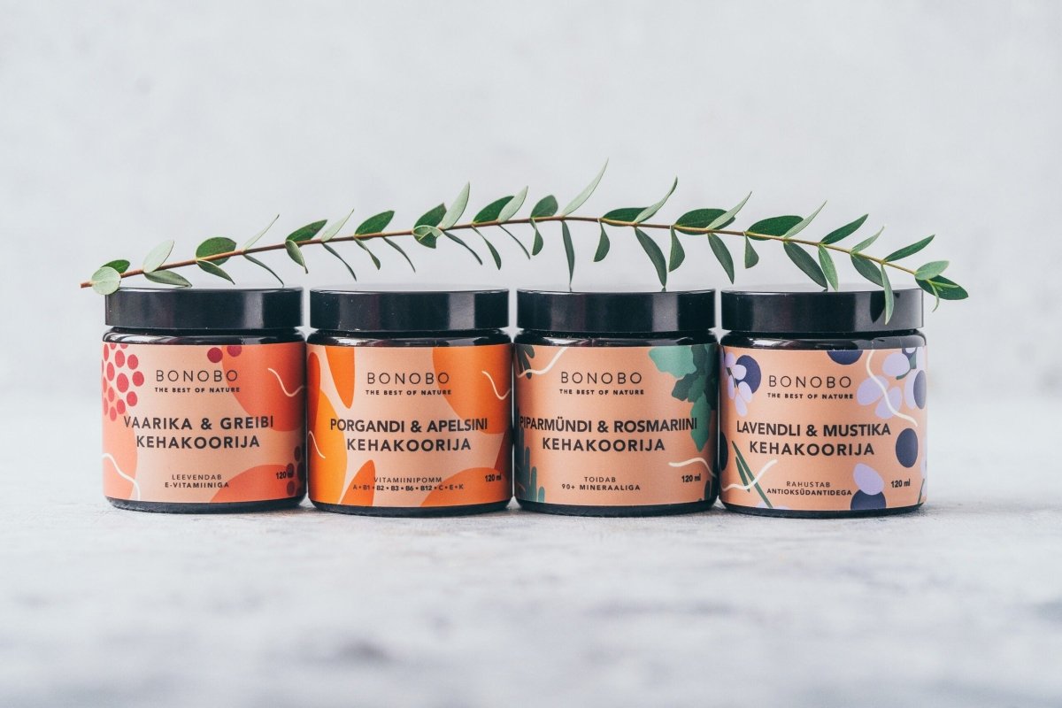 Fyra burkar med naturlig kroppsskrubb från BONOBO i rad, inklusive Body Scrub Blåbär och Lavendel med grön kvist ovanför