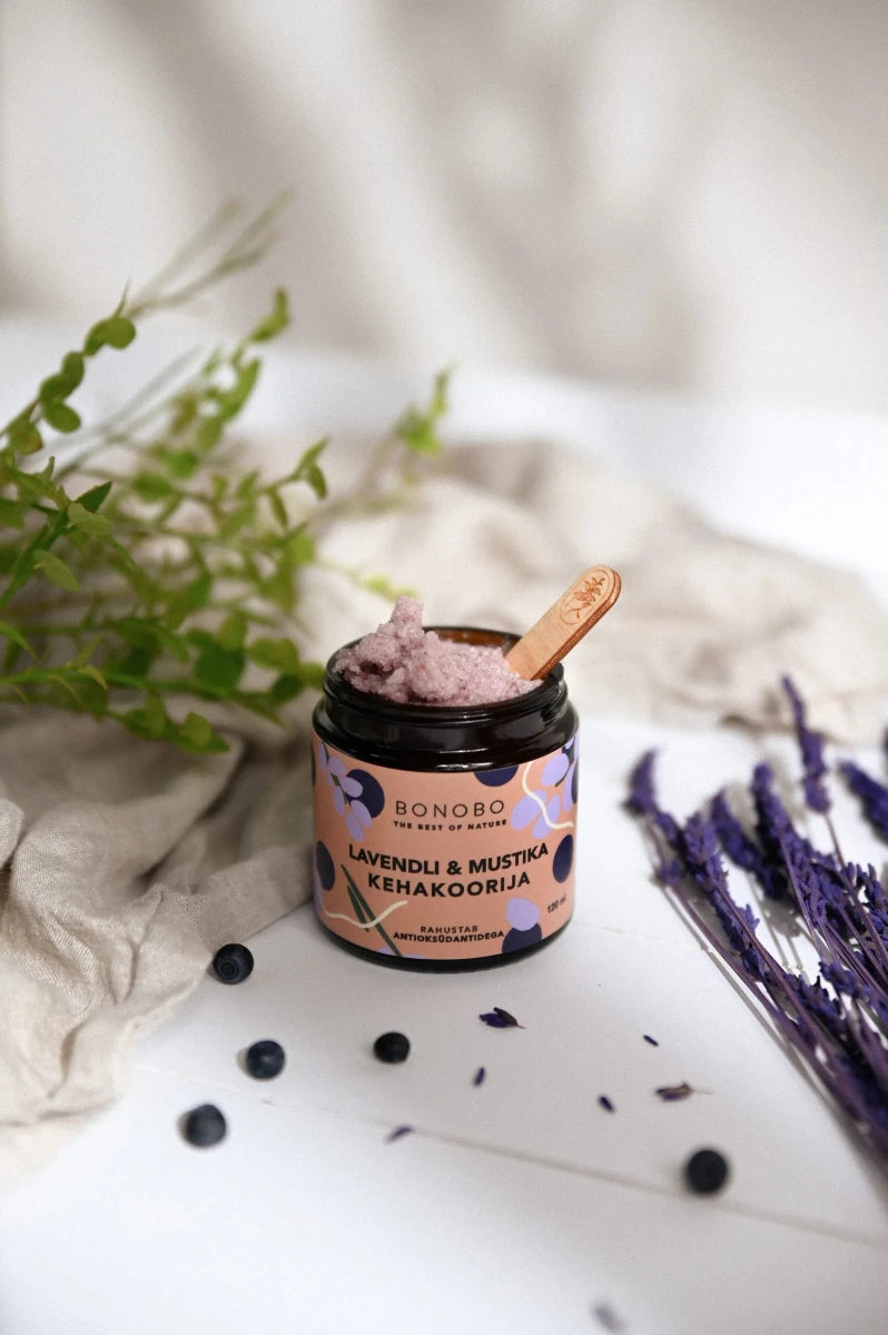 BONOBO Body Scrub blåbär och lavendel i glasburk med träsked, omgiven av lavendel och blåbär i spa-miljö