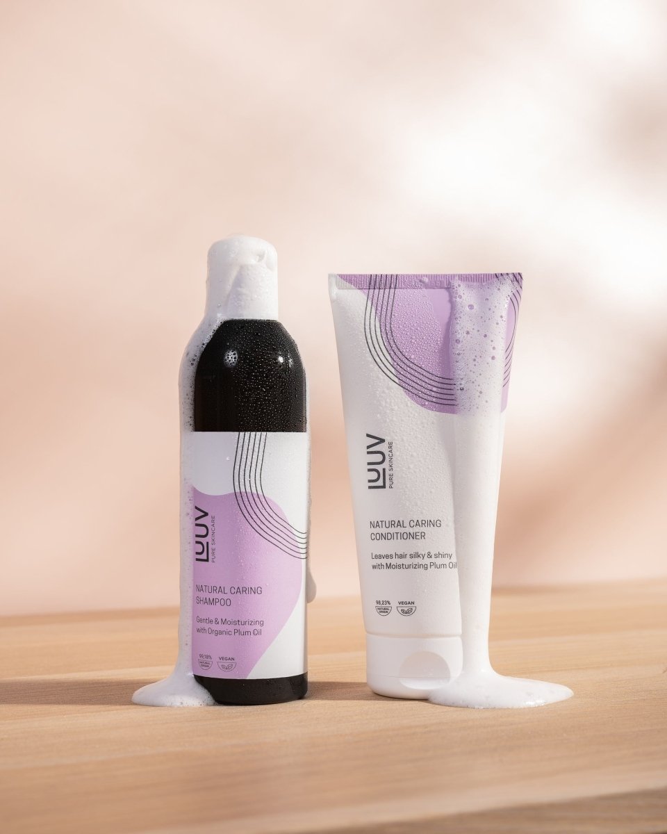 Naturligt schampo och balsam med plommonolja - svart flaska och vit tub med lila designelement på träyta