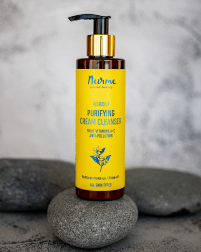 Gul flaska med pumpfunktion innehåller Neroli Purifying Cream Cleanser, placerad på grå stenar mot neutral bakgrund