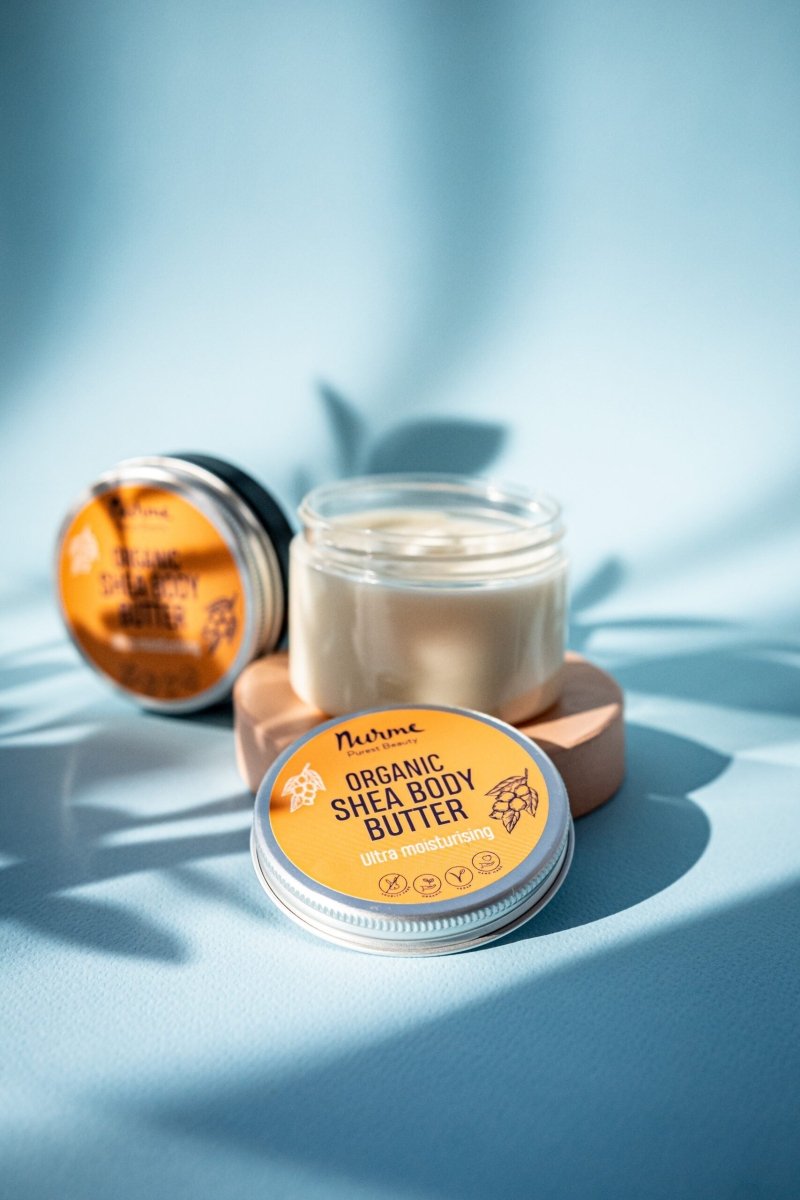 Nurme Organic Shea Body Butter i glasburk med orange etikett, krämig vit textur synlig i öppen burk, blå bakgrund