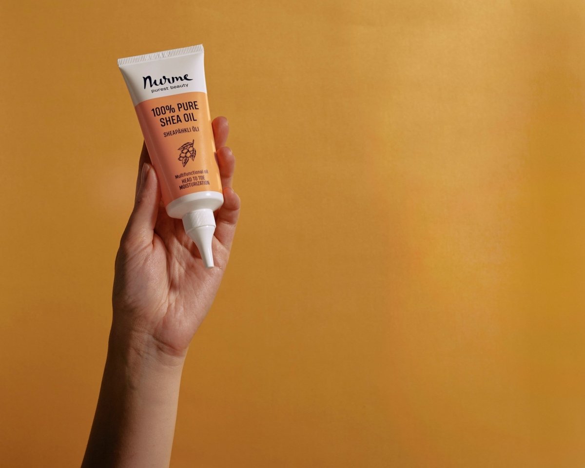 Nurme 100% Pure Shea Oil i orange-vit tub med twist cap-kork, hålls i hand mot orange bakgrund