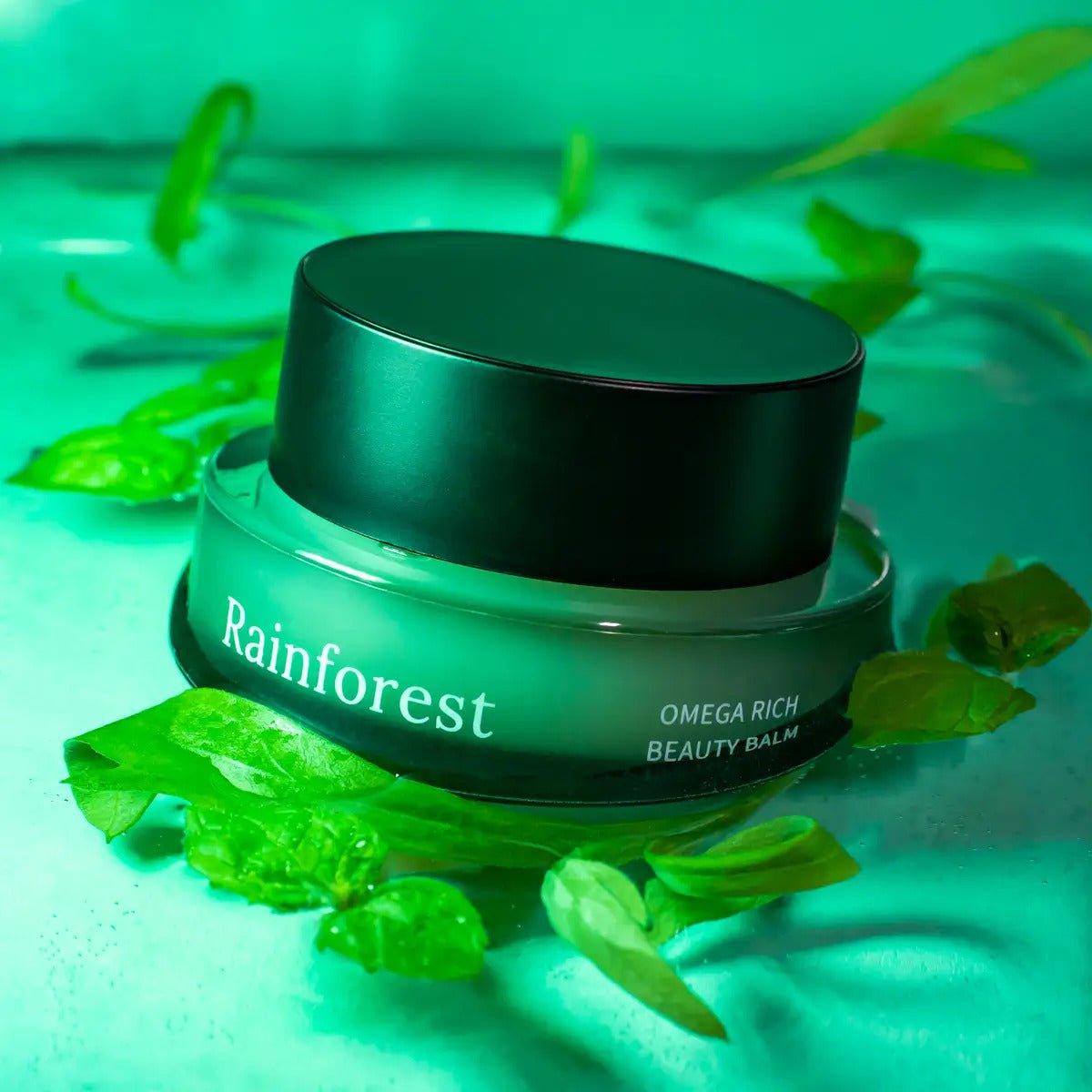 Rainforest Omega Rich Beauty Balm i grön glasburk med svart lock, omgiven av gröna blad i naturlig miljö