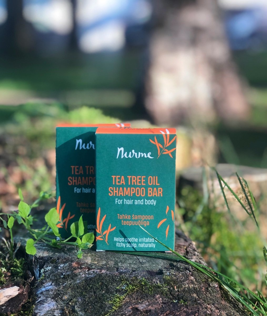 Gröna förpackningar av Nurme schampo mot kliande hårbotten med tea tree på trästubbe utomhus
