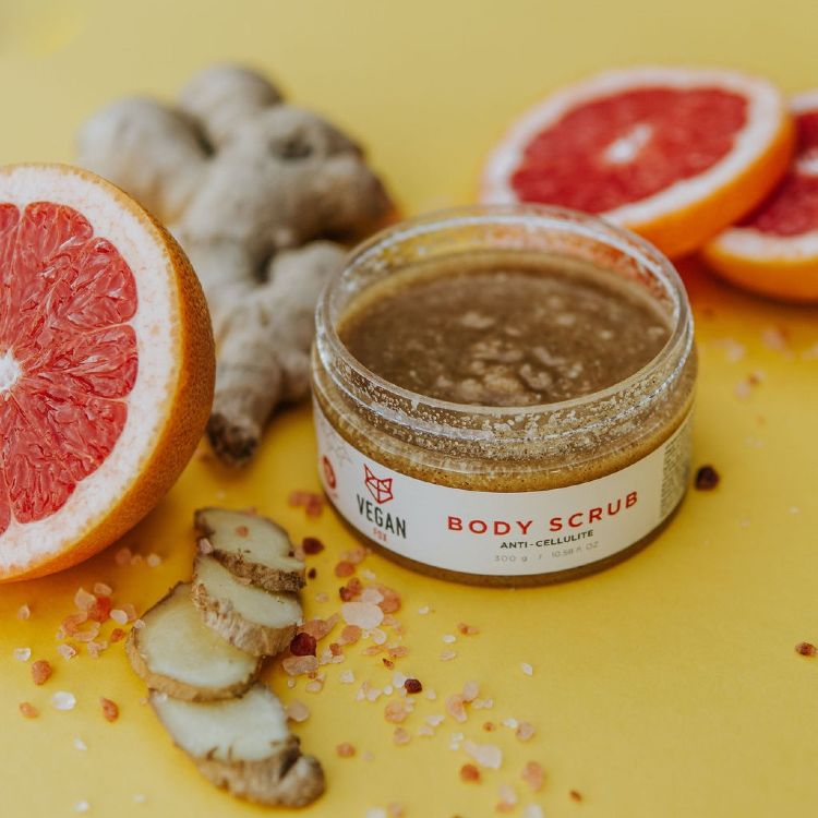 Anti-cellulite Body Scrub Ingefära i glasburk med brun kornig textur, omgiven av färsk ingefära och grapefrukt