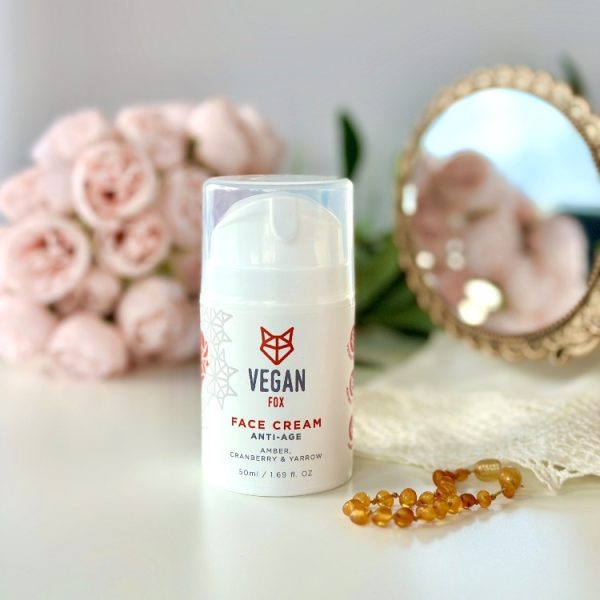 Vit pumpflaska med Vegan Fox Anti-Age Face Cream 50ml på vit yta, omgiven av rosa rosor och gyllene pärlor
