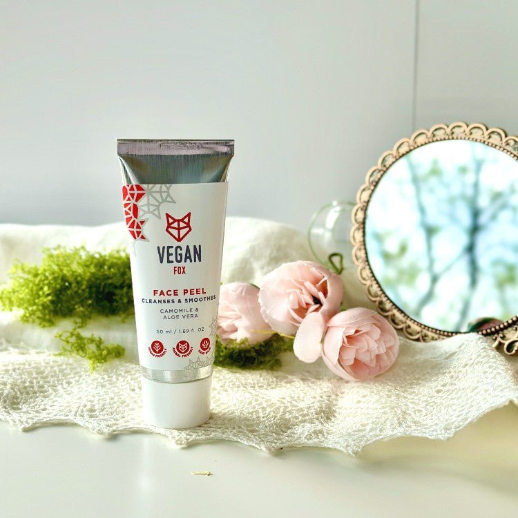 Vegan Fox Face Peel 50ml i vit tub med röd logotyp, omgiven av rosa blommor, spets och spegel på ljus yta
