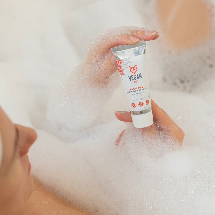 Face Peel 50ml i vit tub med röd text hålls i händer omgiven av bubblor i badkar