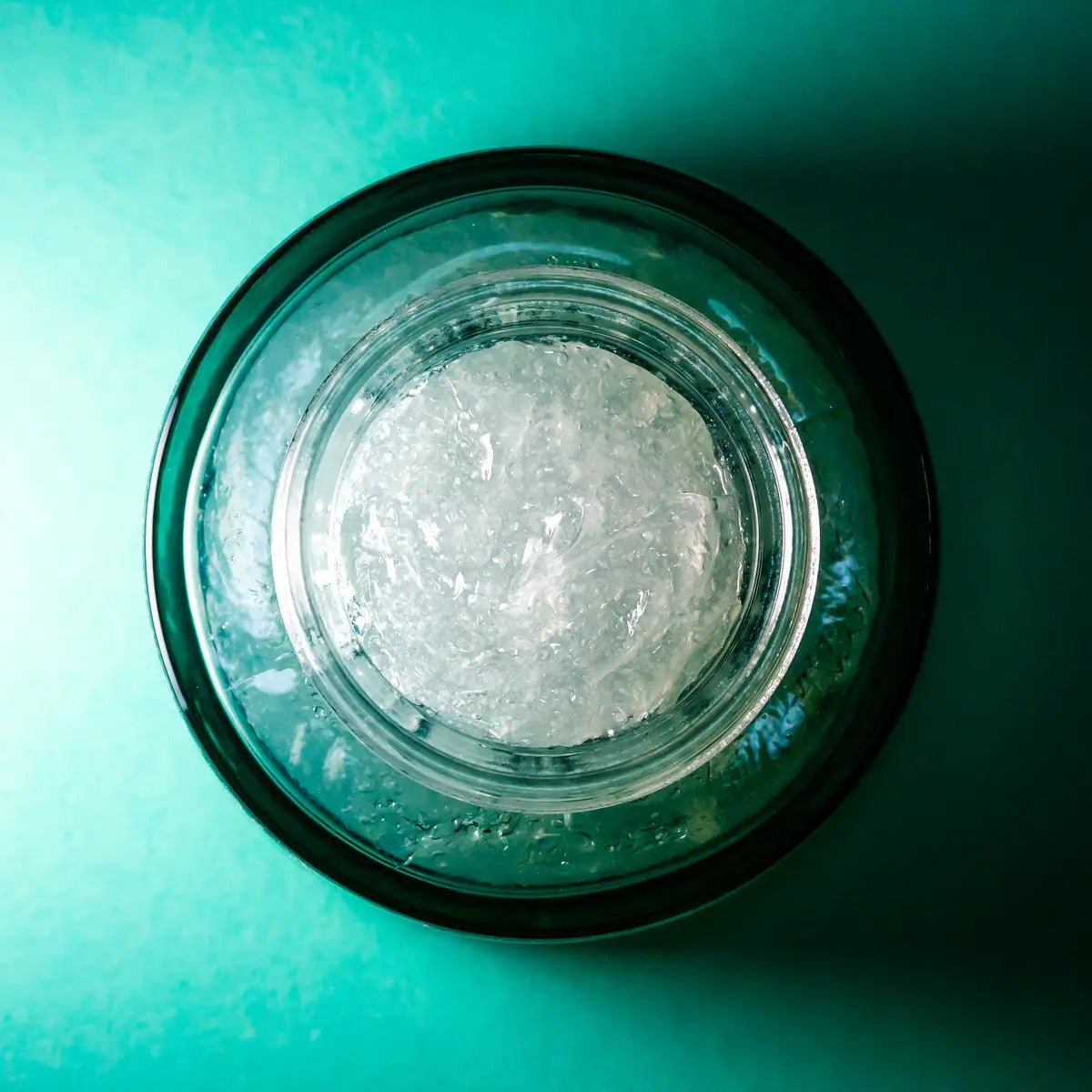 Soft Glow Radiant Exfoliating Jelly i genomskinlig glasburk med geléaktig textur på turkos bakgrund