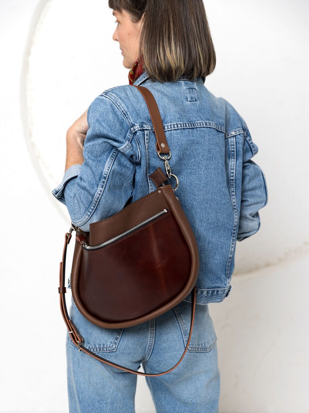 STELLA Leather Handbag i brunt läder med kognacsfärgade detaljer, visad som ryggsäck på kvinna i jeansjacka