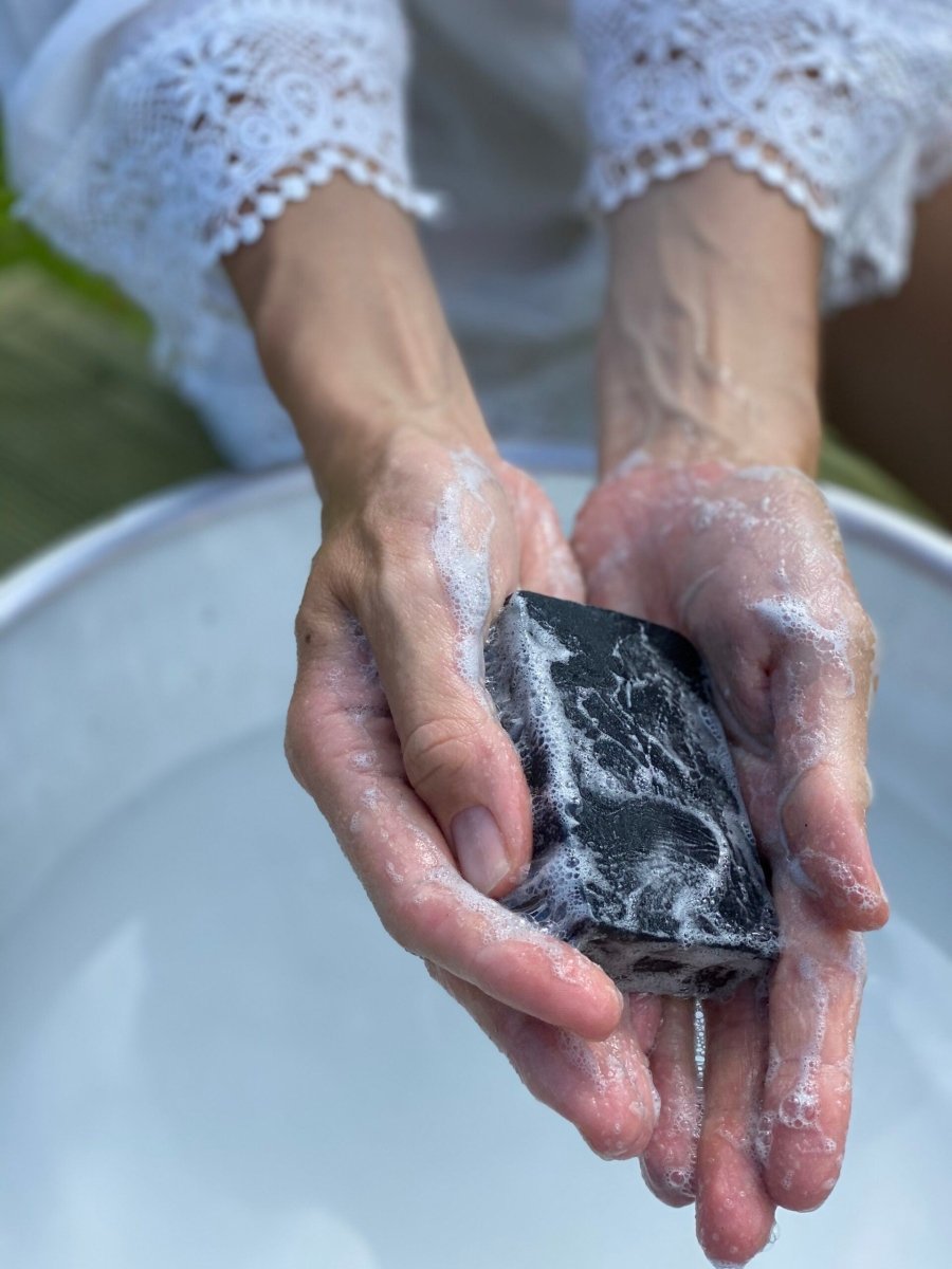 Händer med skum tvättar med Nurmes ansiktstvål med aktivt kol över ett vitt handfat