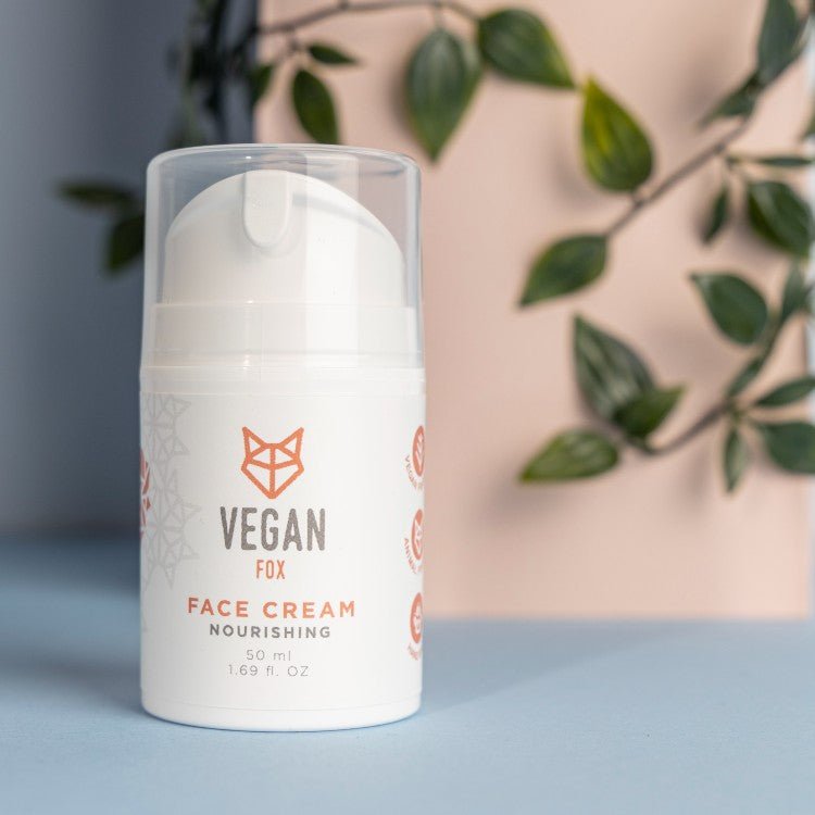 Vit pumpflaska med Vegan Fox Nourishing Face Cream 50ml, genomskinligt lock, stående mot rosa bakgrund med gröna växter
