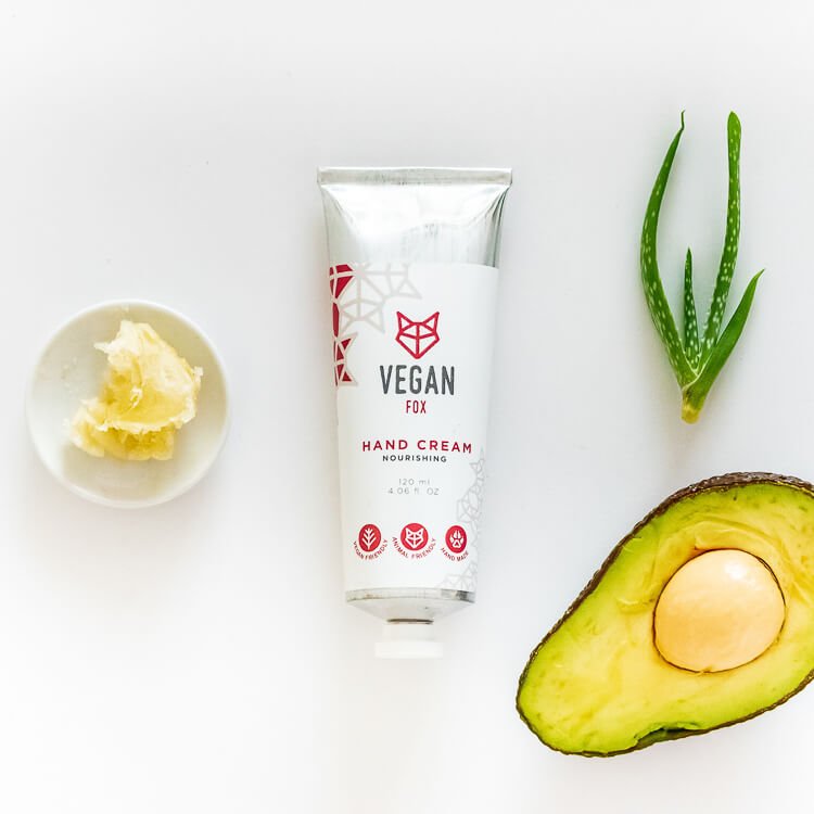 Vit tub med närande handkräm med sheasmör 120ml, omgiven av naturliga ingredienser som avokado och aloe vera