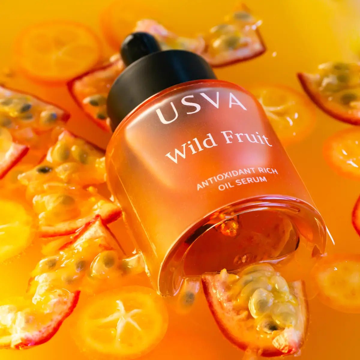 USVA Wild Fruit Antioxidant Rich Oil Serum i orange glasflaska omgiven av passionsfrukt och tropiska frukter