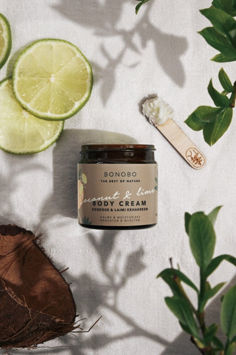 BONOBO Body Cream kokos och lime i brun glasburk omgiven av limehalvor, kokosnöt och gröna blad på vit textilbakgrund