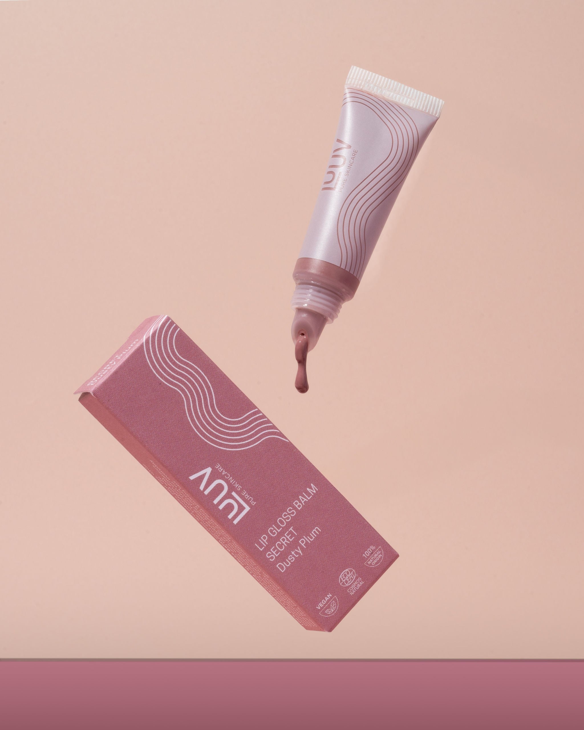LUUV Lip Gloss Balm Secret i rosa tube med droppande produkt och matchande förpackning mot rosa bakgrund