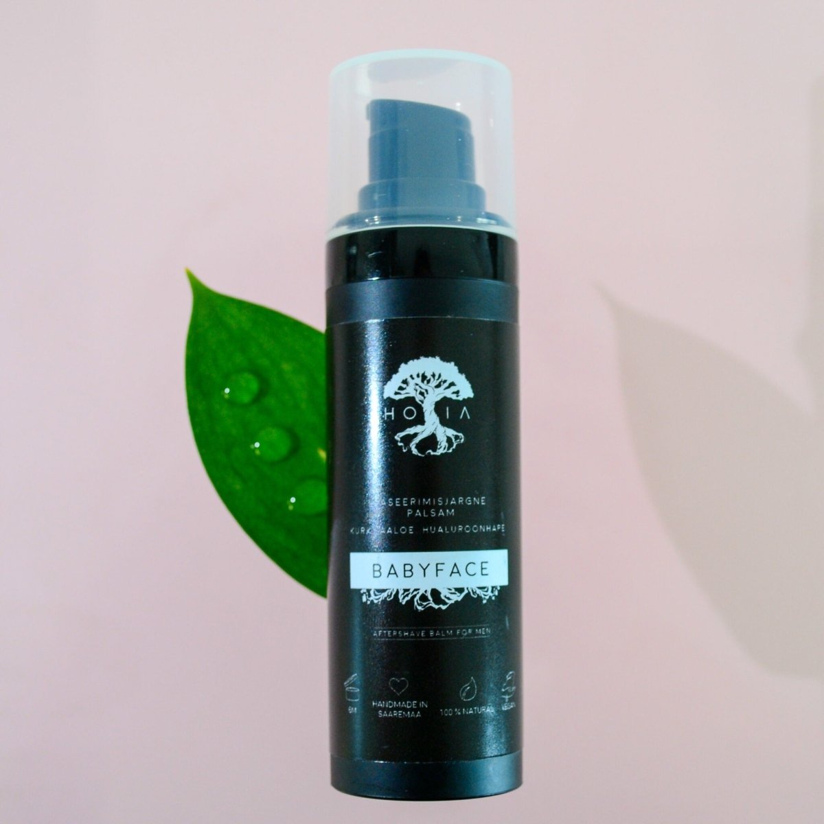 HOIA Babyface aftershave balm för män – svart pumpflaska mot rosa bakgrund med grönt blad