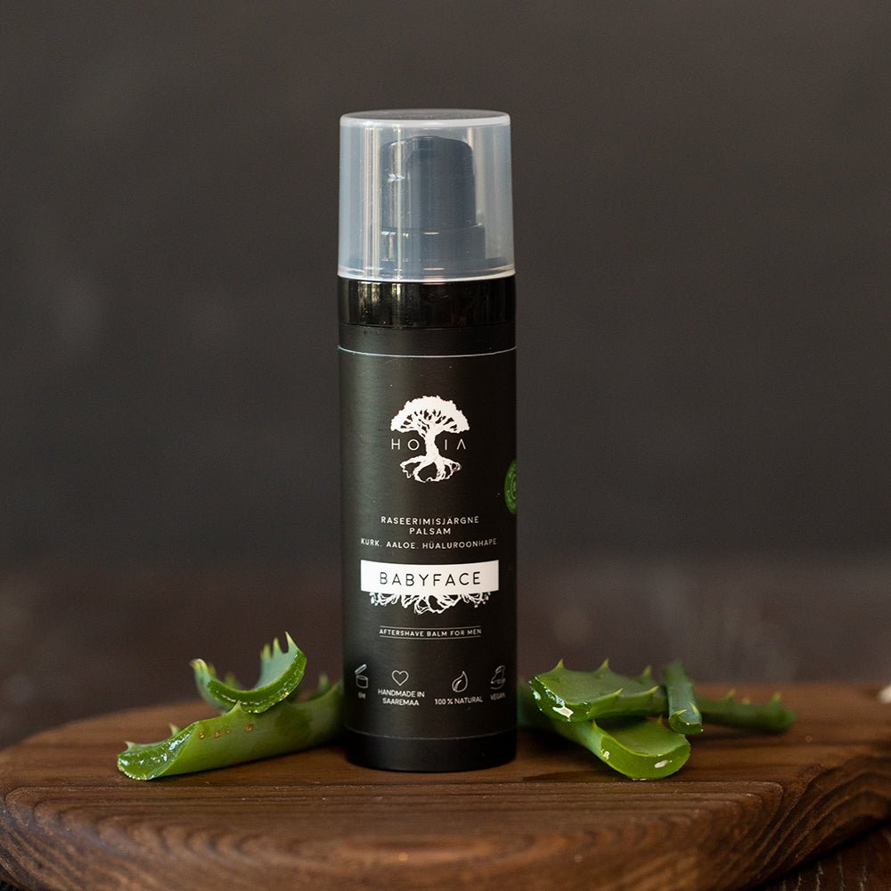 HOIA Babyface aftershave balsam för män i svart flaska omgiven av färska aloeverablad på träunderlag