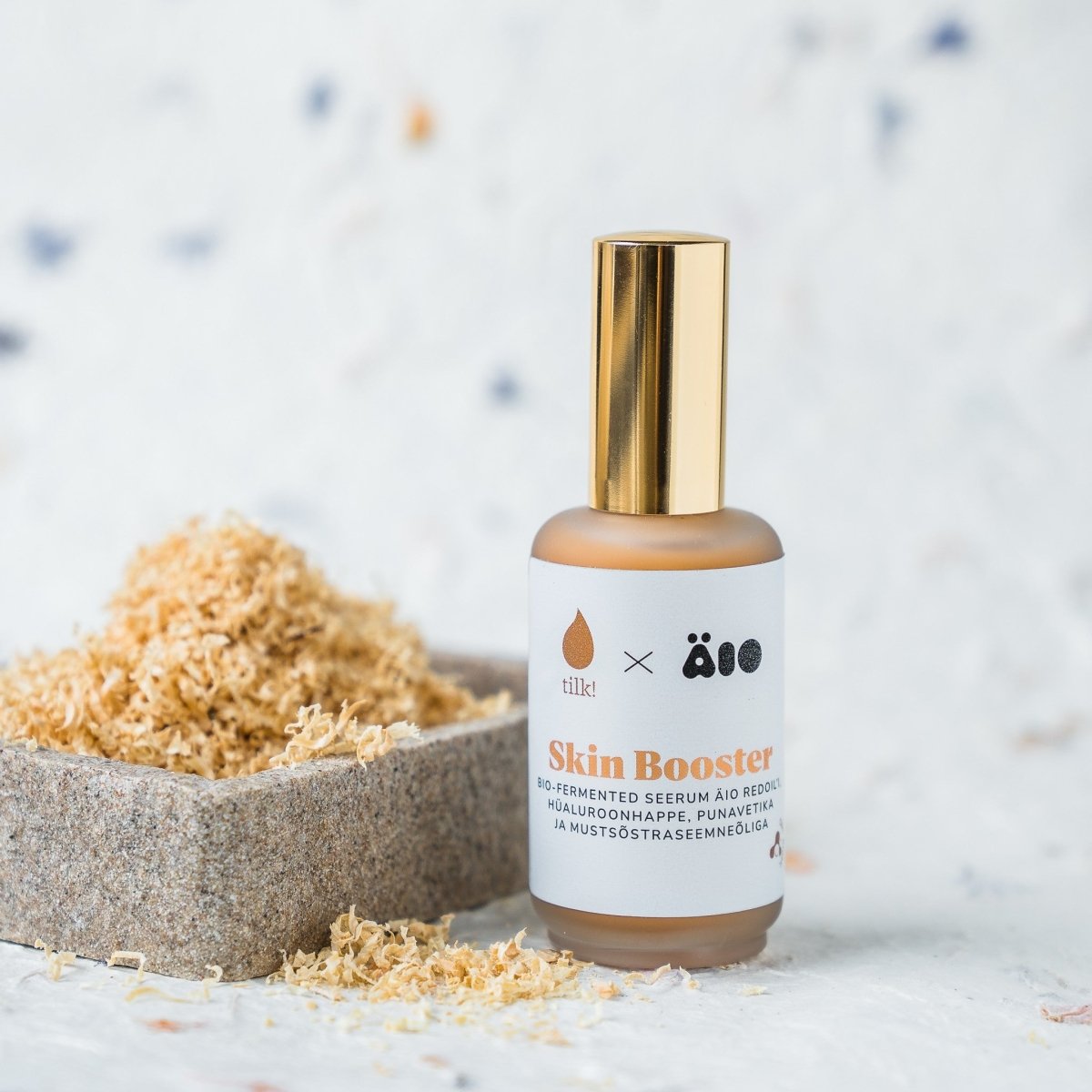 Ansiktsserum naturligt Skin Booster i brun flaska med guldpump, bredvid träflis