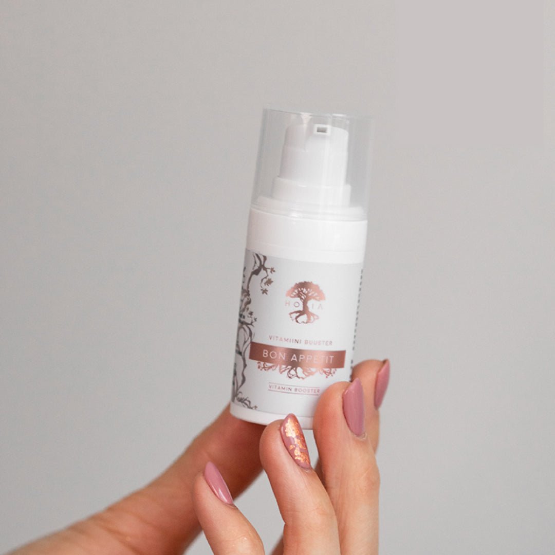 Vit pumpflaska med Bakuchiol Vitamin Serum Bon Appétit hålls i hand med rosa naglar mot ljus bakgrund