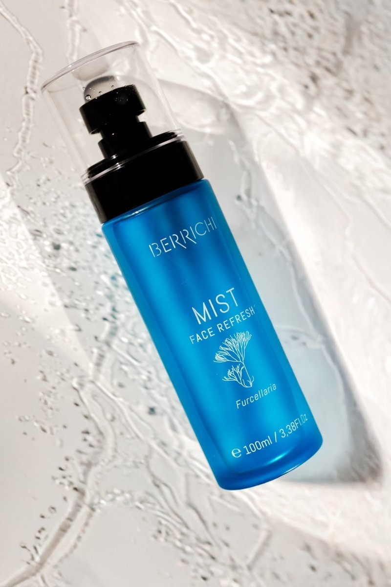 Blå glasflaska med pump-spray innehållande MIST Face Spray 100ml från BERRICCI, fotograferad mot vit texturerad bakgrund