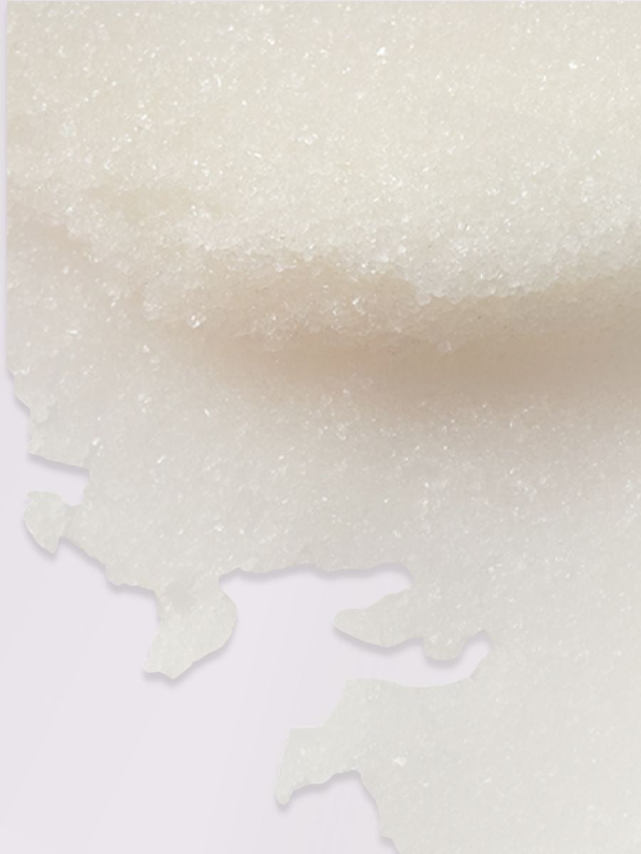 Body Scrub med Pionarom - krämvit exfolierande textur med glittrande partiklar utsmeten på vit yta