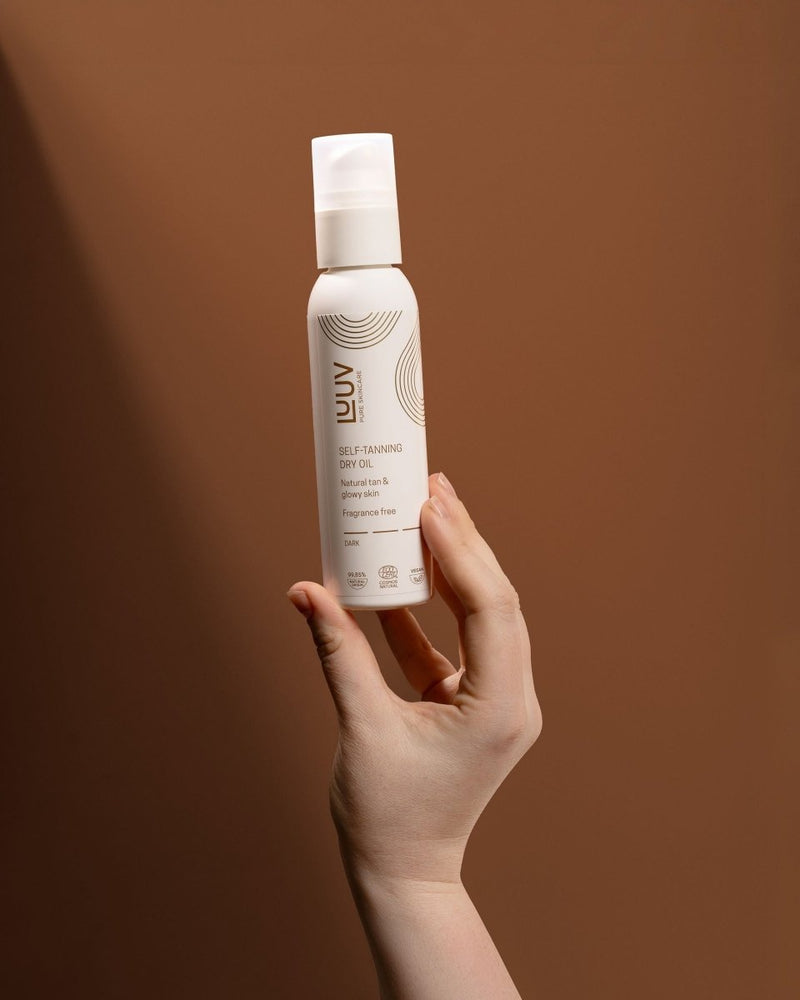 Vit sprayflaske med Brun Utan Sol Torrolja - Mörk 150ml hålls i hand mot brun bakgrund, elegant designad förpackning