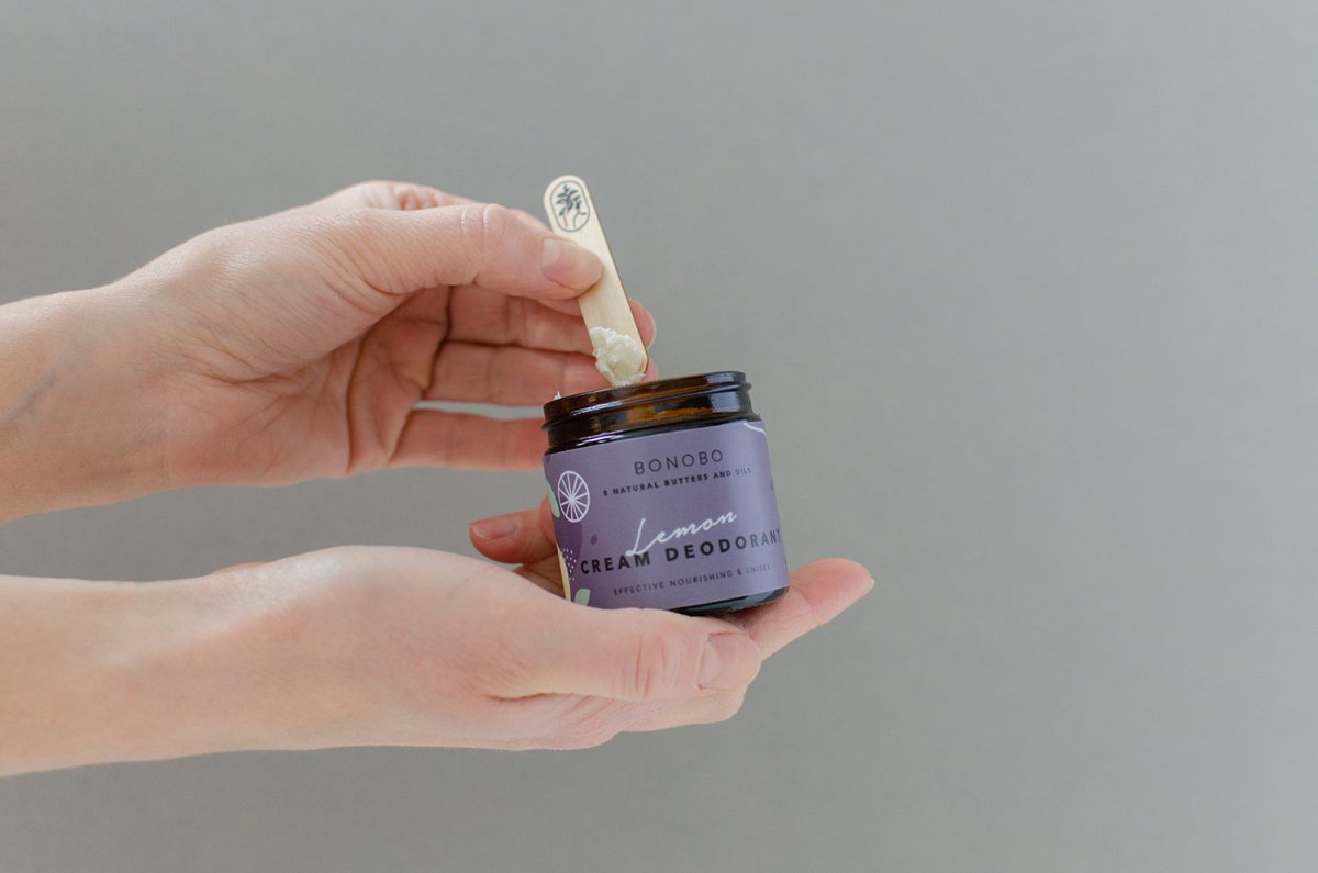 Händer håller lila glasburk med Bonobo deodorantkräm lavendel och träsked med vit krämig textur
