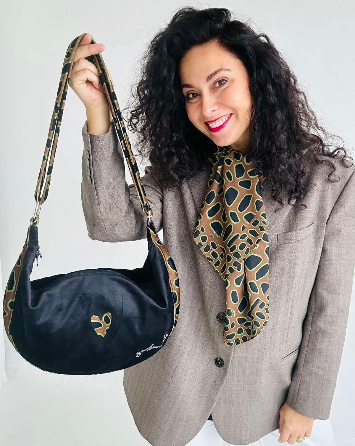 Hobo Bag - Leopard Heart i mörkblått läder med leopardmönstrat hjärta och matchande axelrem, hålls upp av kvinna i grå kavaj