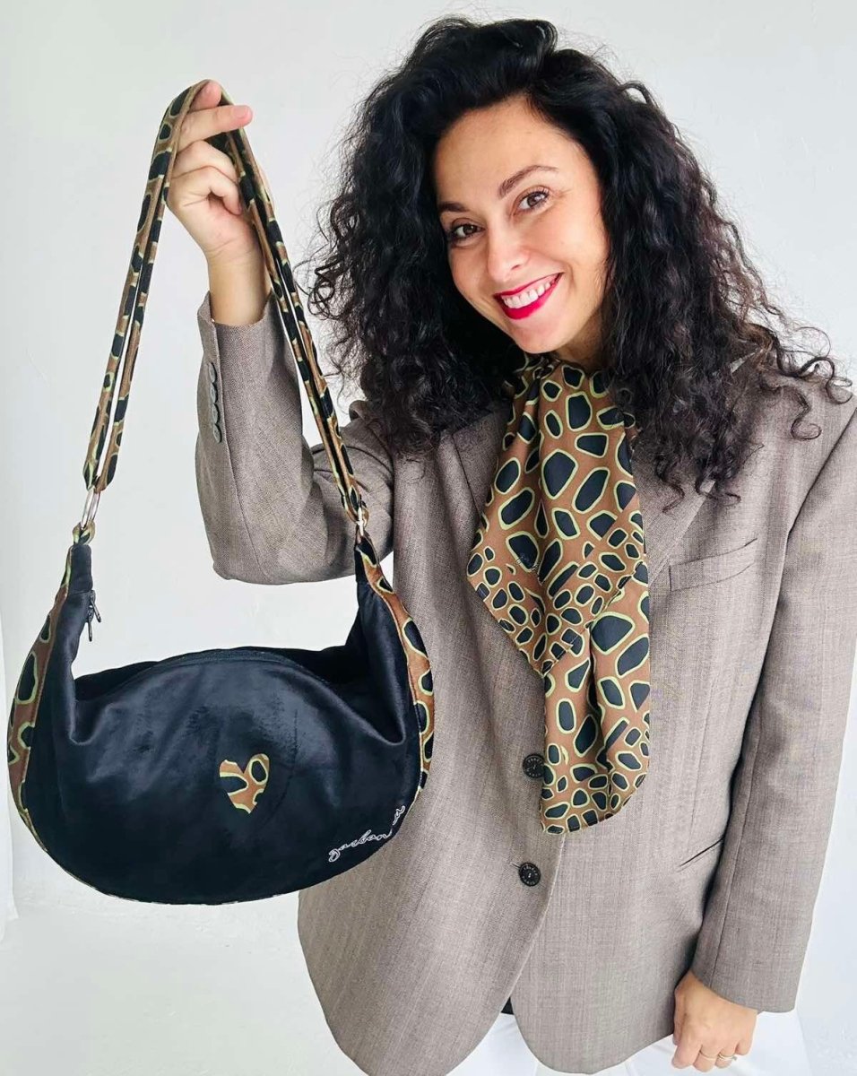 Hobo Bag - Leopard Heart i mörkblått läder med leopardmönstrat hjärta och matchande axelrem, hålls upp av kvinna i grå kavaj