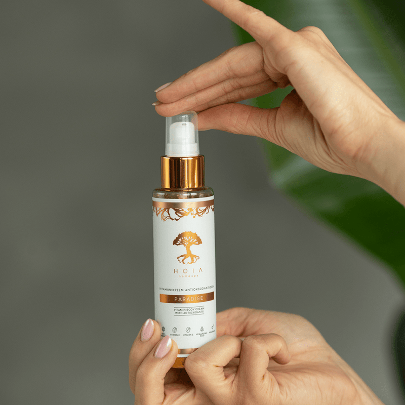 Händer håller pumpflaska HOIA Paradise kroppskräm torr hud med hyaluronsyra och C-vitamin, 100 ml