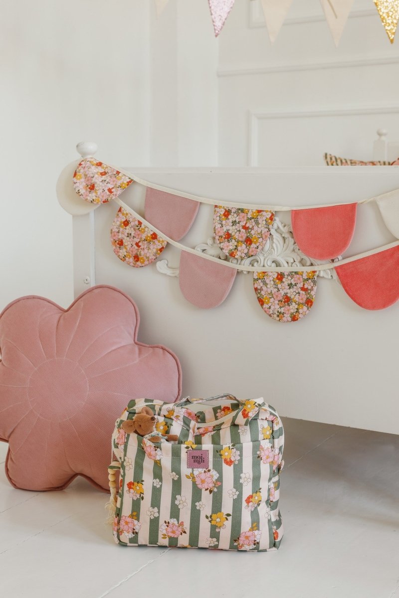 Large Make-Up Bag Green Striped - grönvitrandig necessär med blommönster, står på vitt golv bredvid rosa kudde