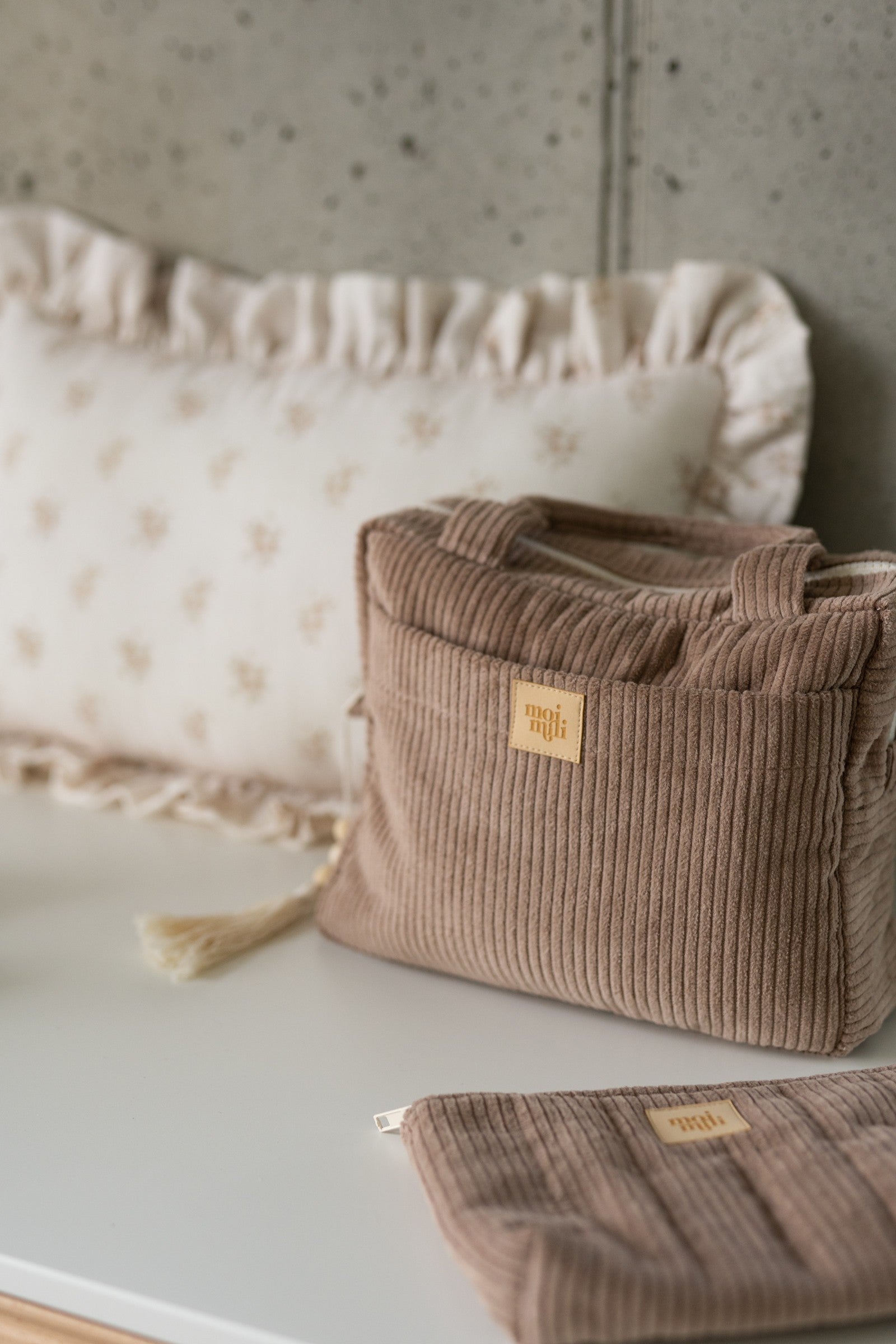 Large Make-Up Bag Latte i beige manchestertyg med guldlogga, stående på vit säng med matchande necessär