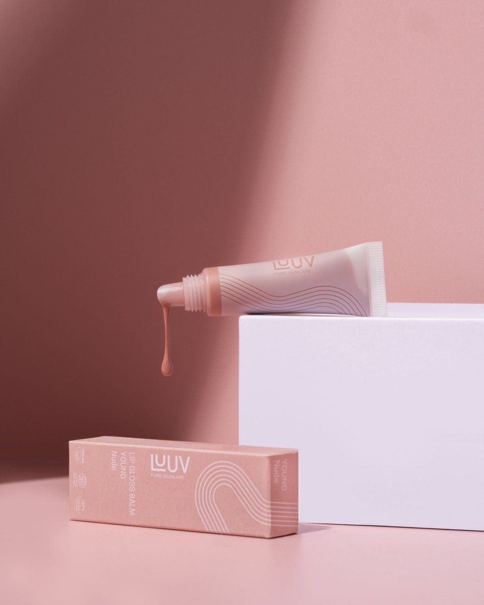 Läppbalsam Young i rosa tub med vågmönster, droppar av produkt och matchande förpackning på vit piedestal