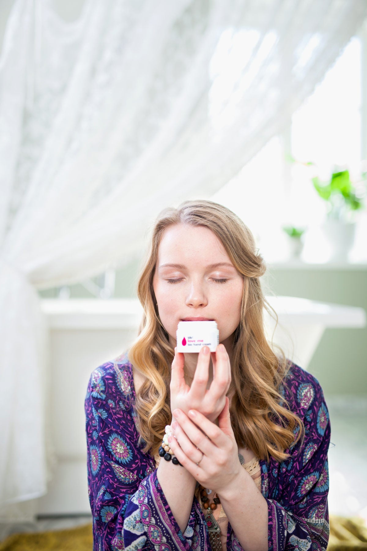 Kvinna håller och luktar på vit handkräm Love Me med mango och citrongräs i ljust kök