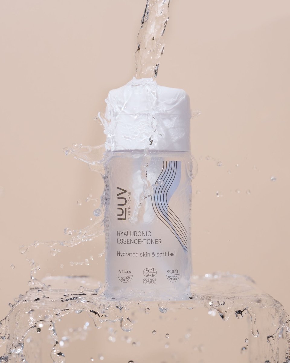 LUUV Hyaluronic Essence-Toner i transparent flaska med vit pump, omgiven av vattenstänk mot beige bakgrund