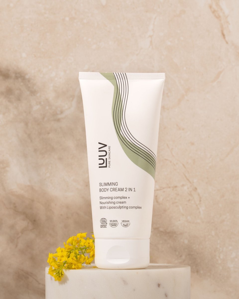Vit tub med LUUV Slimming Body Cream 2 in 1, elegant grön-svart vågtryck, COSMOS-märkt, bredvid gul blomma på marmor