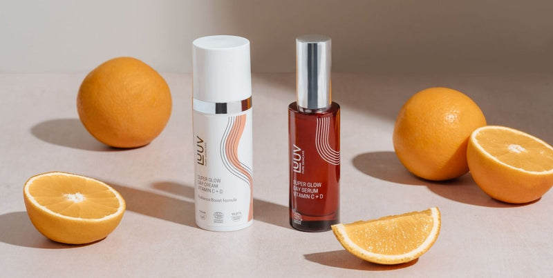 LUUV Super Glow Day Cream i vit pump-flaska med silver detaljer, omgiven av apelsiner på beige bakgrund