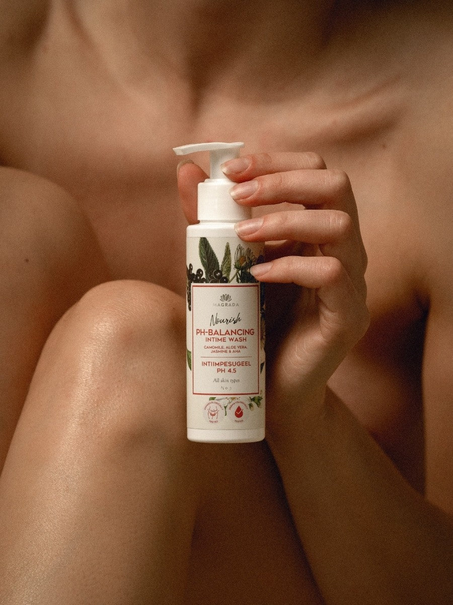 Magrada intimduschgel med kamomill och aloe vera i vit flaska med pump, hålls i hand mot naturlig bakgrund