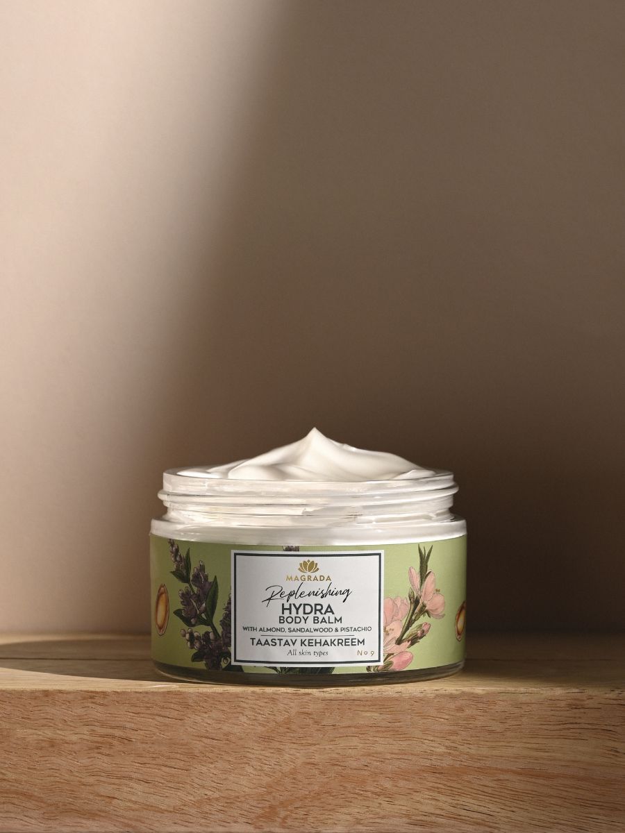 Magrada Replenishing Body Balm i grön burk med blommönster, öppen med vit krämig textur synlig, på trä