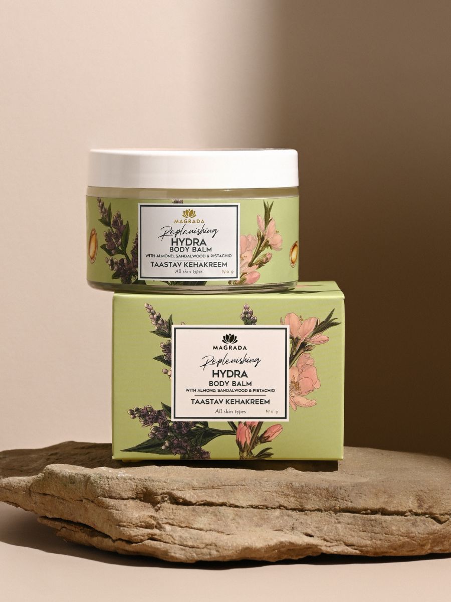 Magrada Replenishing Hydra Body Balm i grön förpackning med blommotiv, vit burk och matchande kartong på träyta