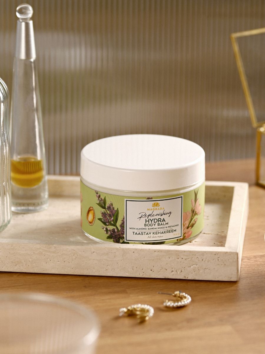 Magrada X Lauren Replenishing Body Balm i vit burk med grön etikett, placerad på marmorbricka med glasflaska