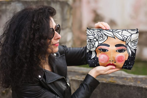 Kvinna håller upp MAKEUP BAG YOKO BLACK - svart necessär med färgglatt ansiktsmotiv, rosor och prickar