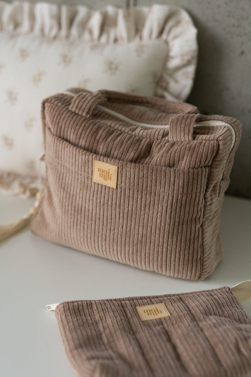 Manchesterset med två makeup-väskor i latte-beige färg, ribbad textur och guldiga märkeslappar på vit bakgrund