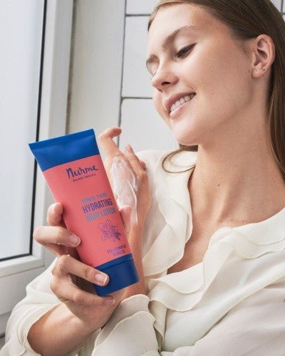 Kvinna ler och applicerar Monoi kroppslotion naturlig på handen från rosa tub