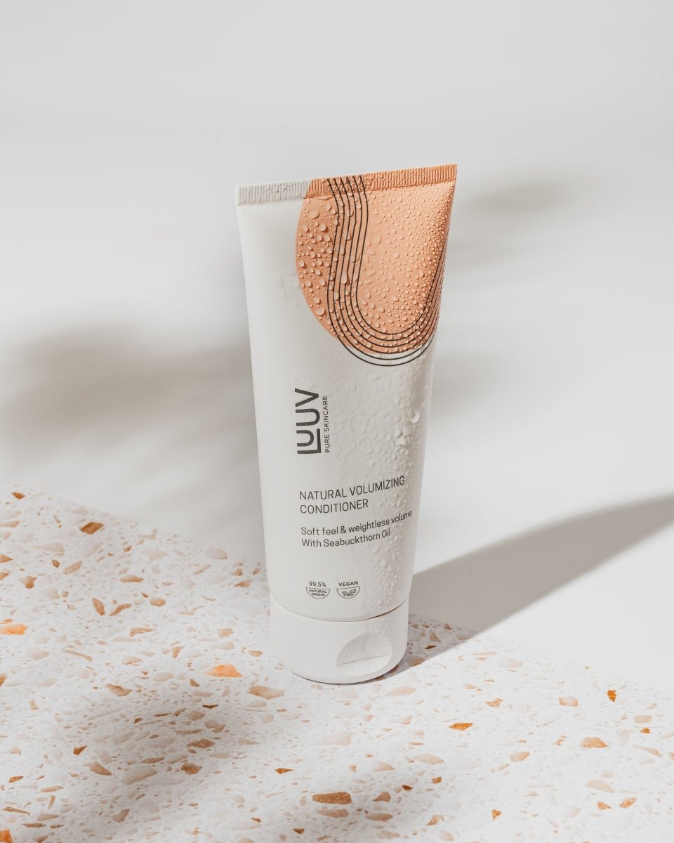 Vit tub med orange dekorativa element innehåller naturligt havtornsbalsam 200ml, stående på marmoryта