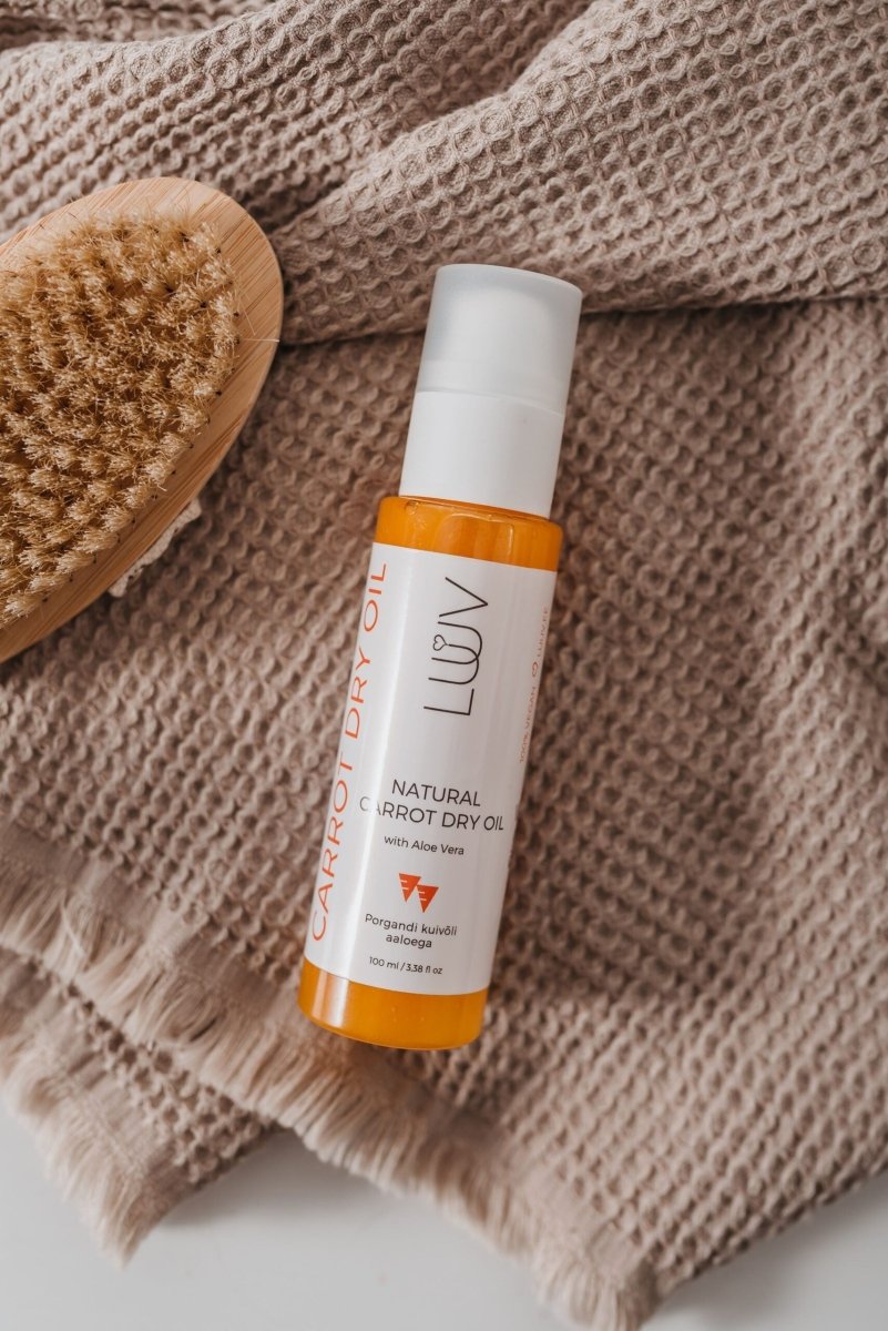 Naturlig Carrot Dry Oil med Aloe Vera i vit flaska med orange innehåll och pumpspray, bredvid naturlig borste