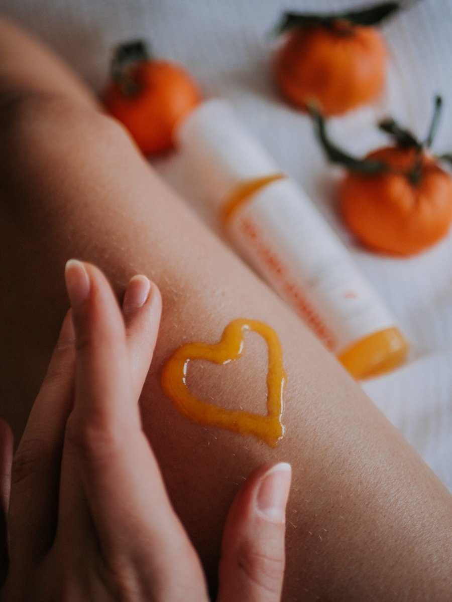 Naturlig Carrot Dry Oil med Aloe Vera applicerad i hjärtform på arm, omgiven av apelsiner och vit flaska