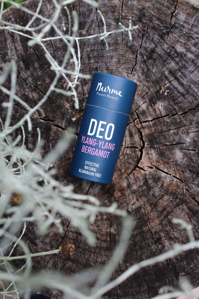 Blå cylinderformad deodorantstick från Nurme med texten DEO Ylang-Ylang Bergamot på trädstubbe omgiven av torra grenar